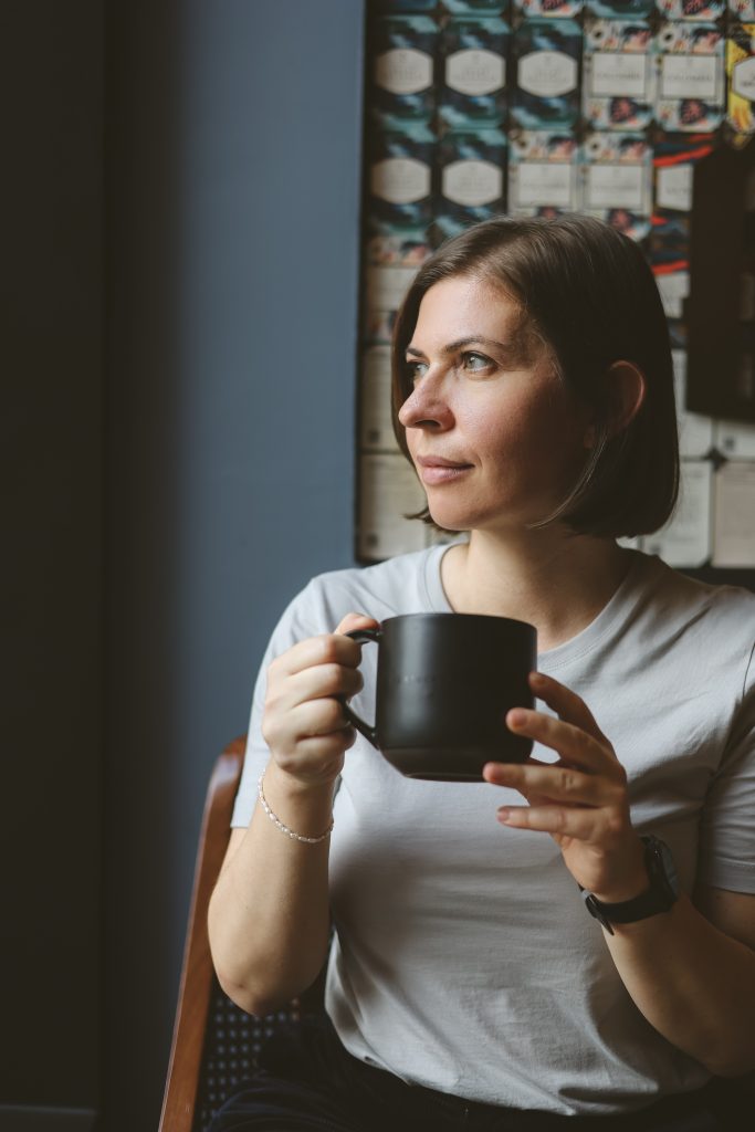 Person sitting by a window holding a black mug and looking outside in a calm, relaxed atmosphere.